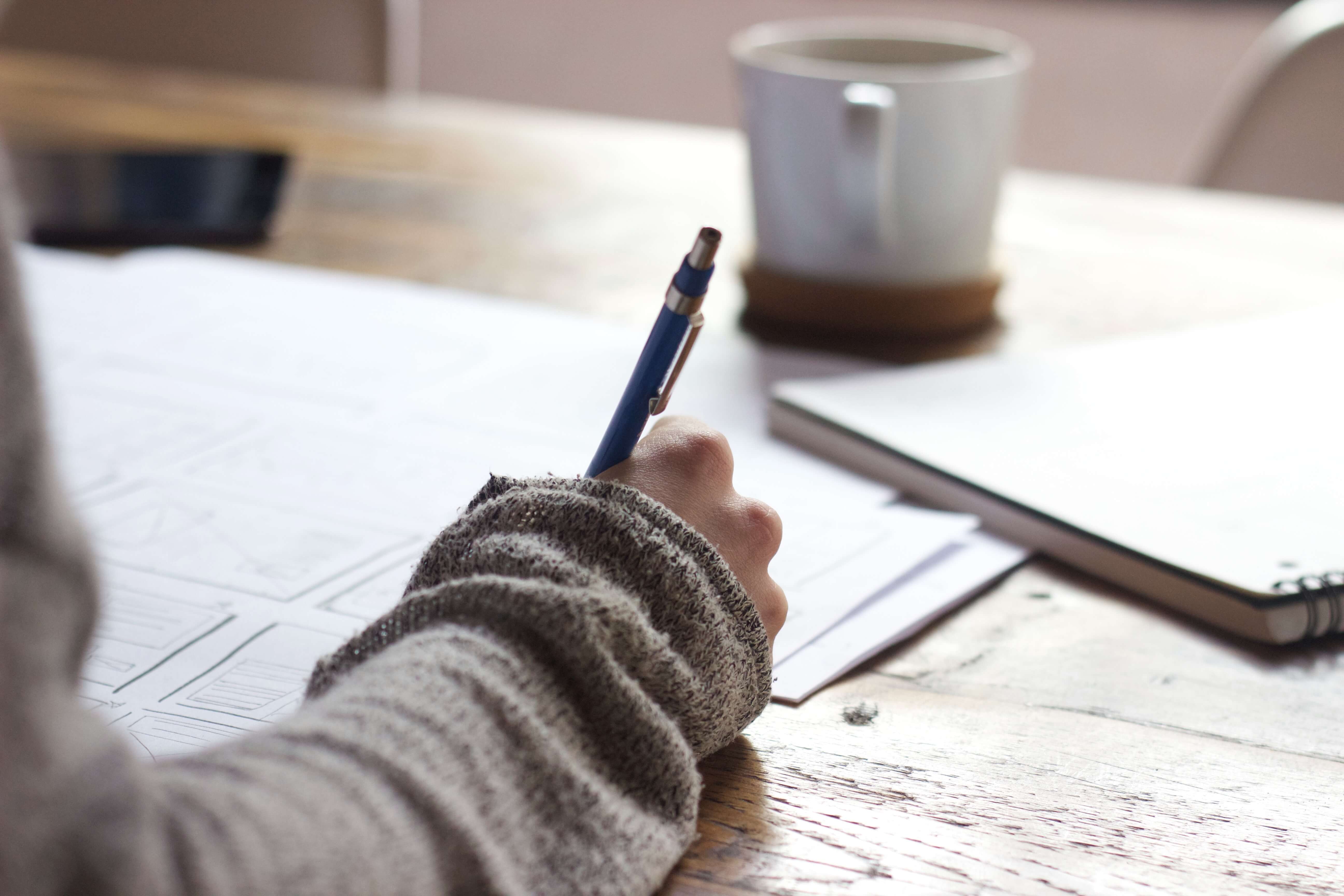 Close up of someone writing with a gray sleeve and a blue pen.