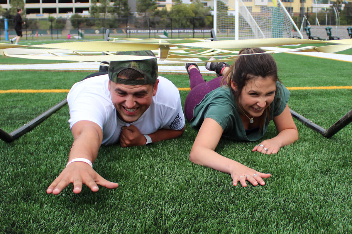 Male and female student on grass participating in an army crawl obstacle