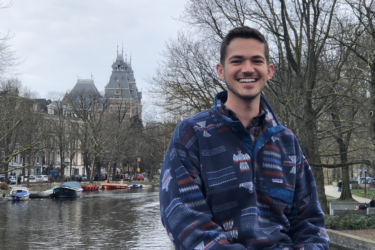 Mark Borges smiles while sitting in front of a river in Amsterdam
