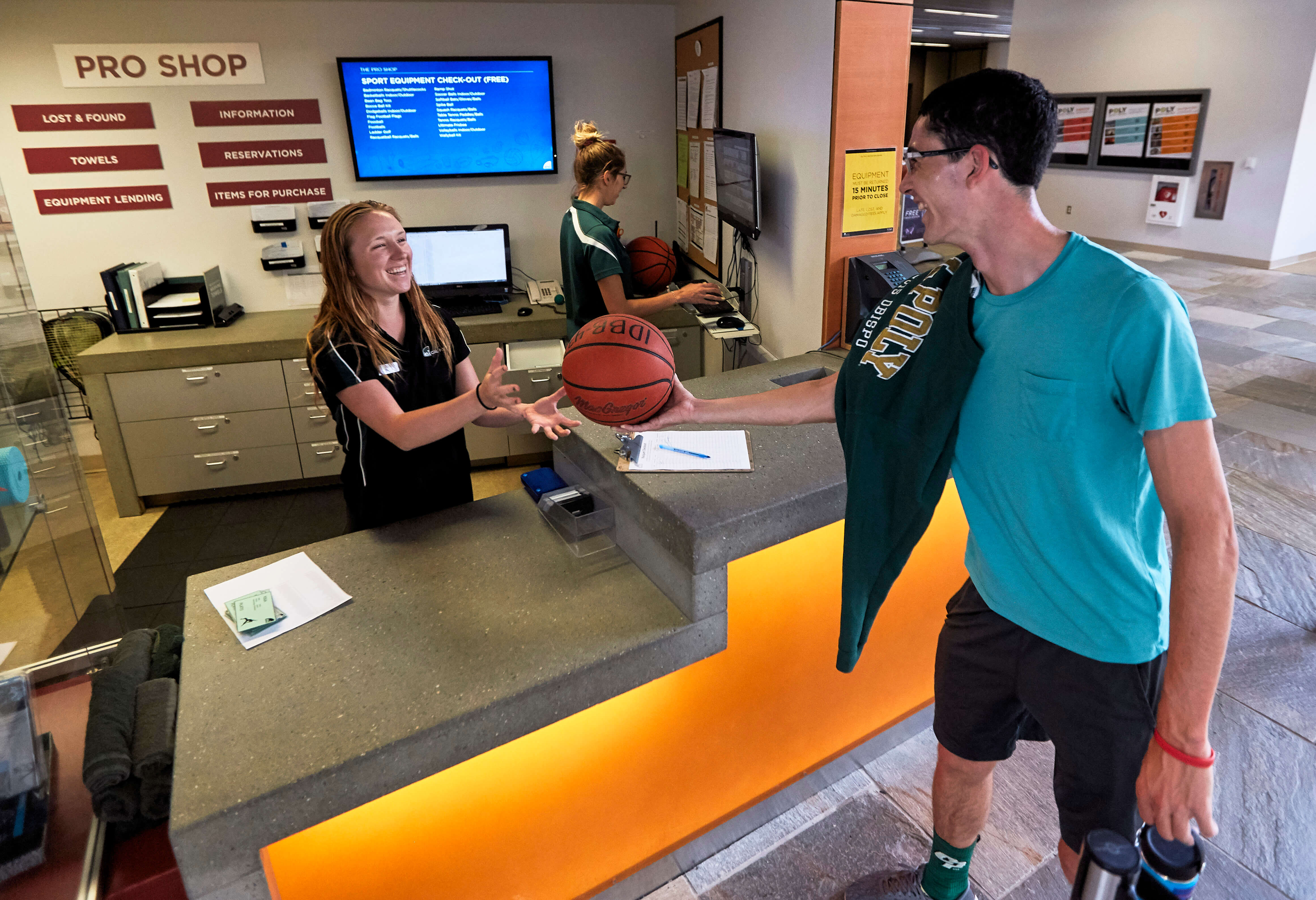 A male student smiles while handing a basketball to a female employee at The Pro Shop