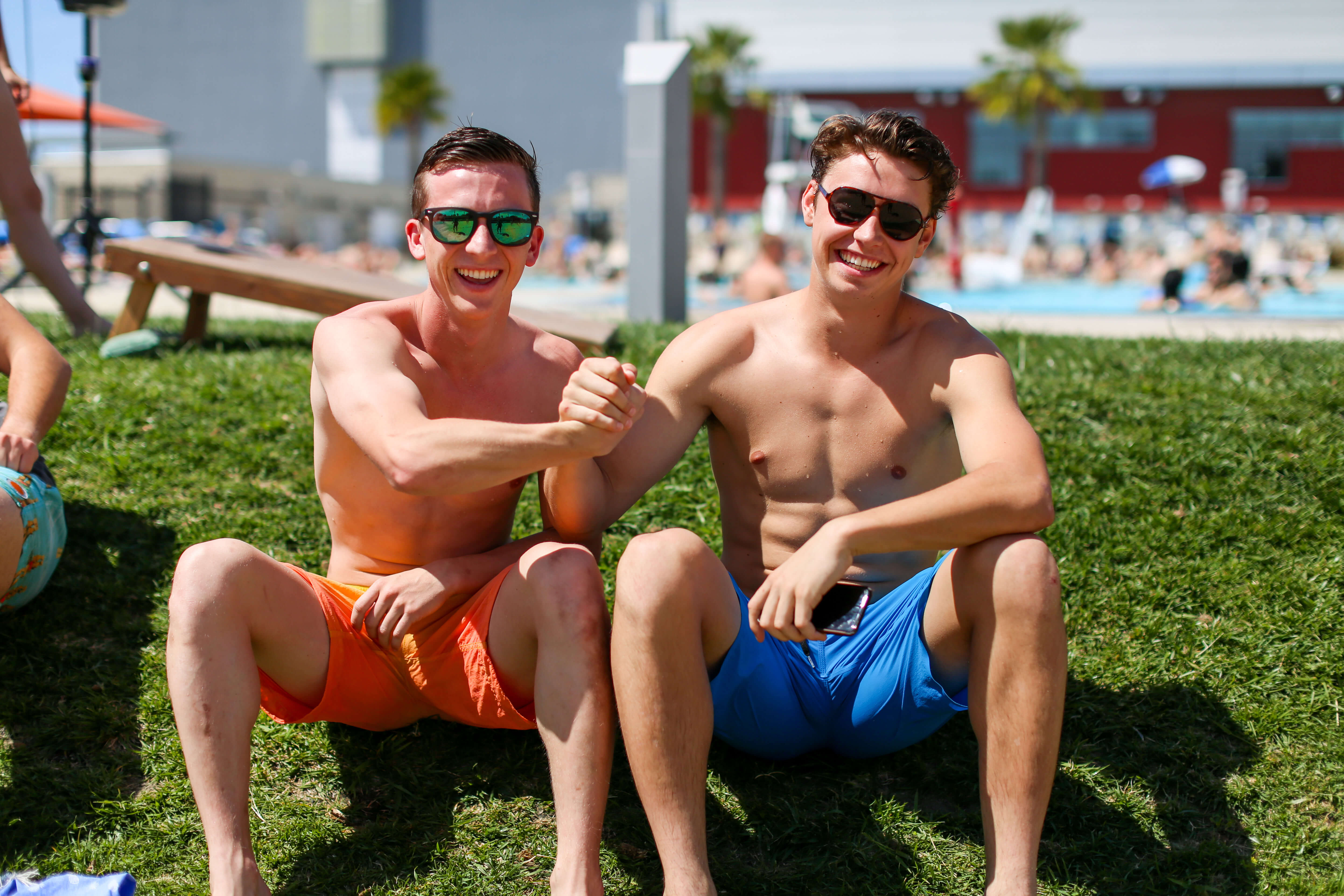 Two male students smile in front of the pool wearing sunglasses and joining hands 