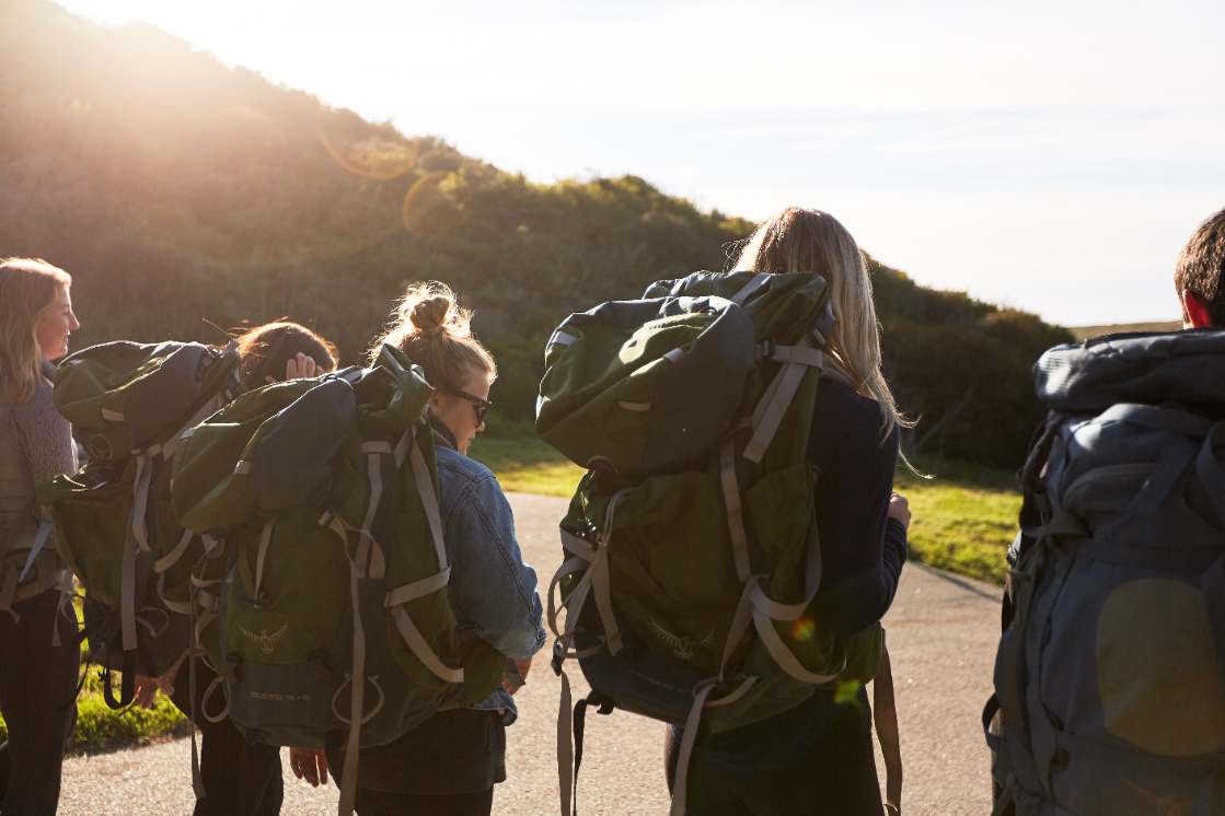 Students wearing backpacks hiking off toward a green hill