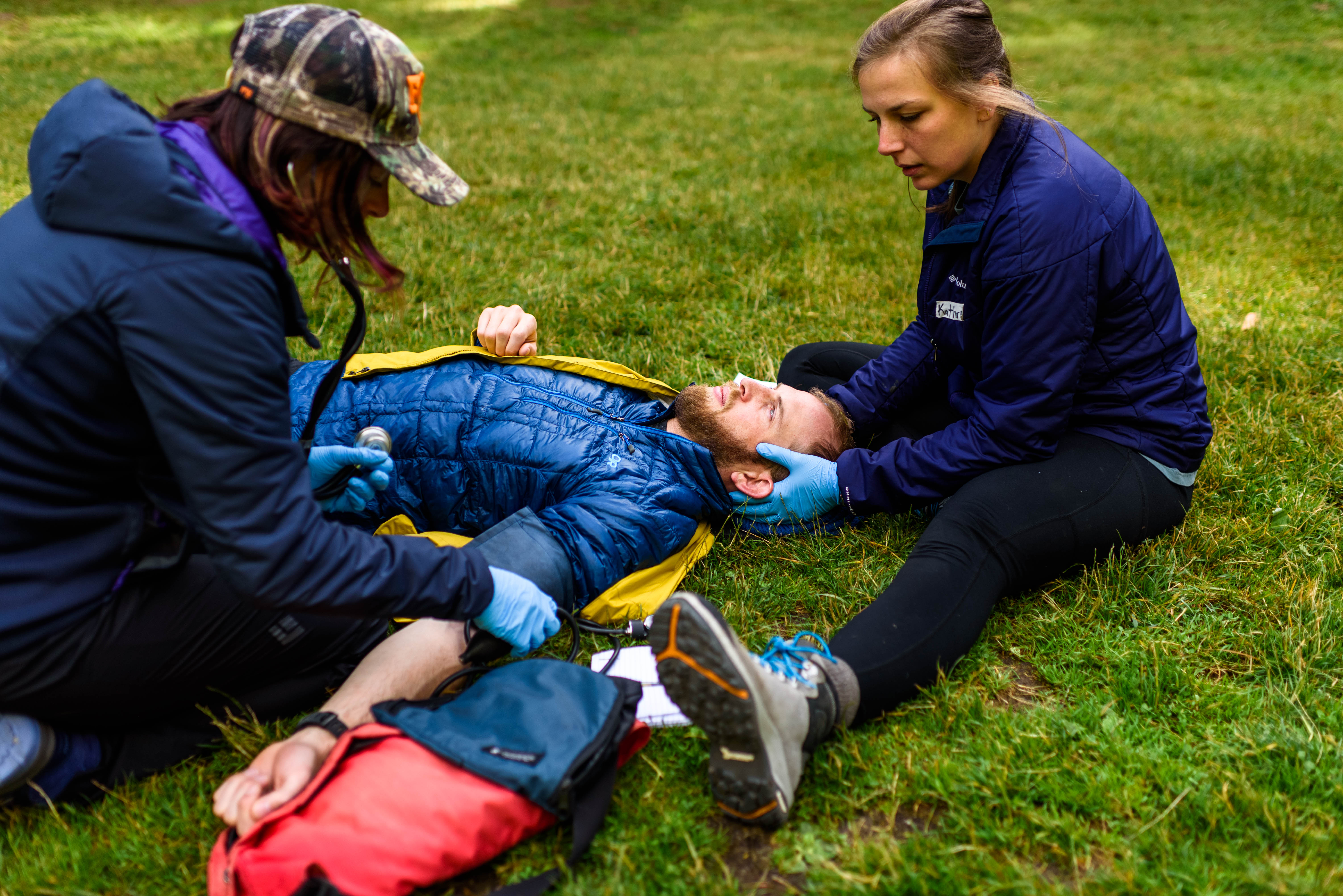 Two class participants examine and check the blood pressure of a male participant on the ground